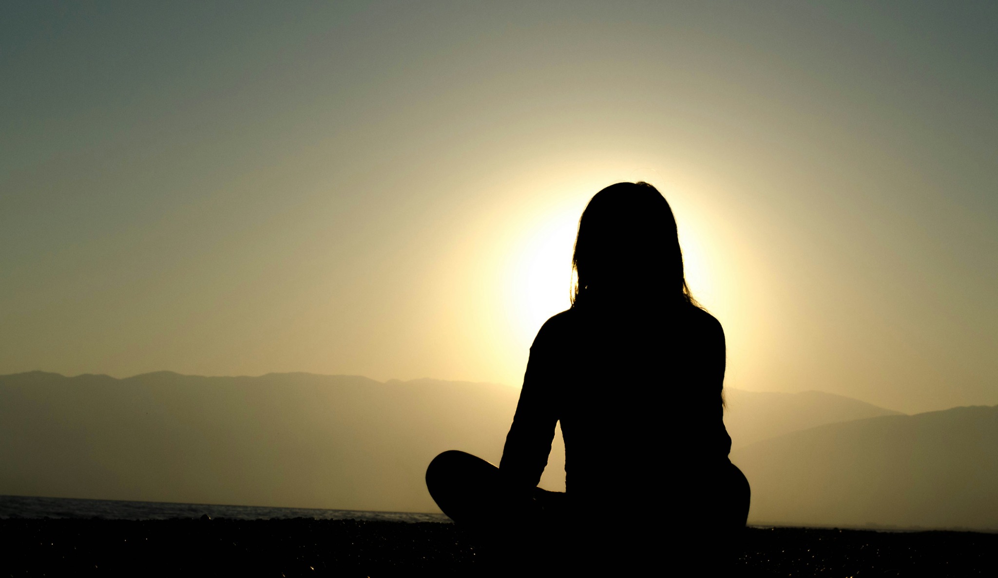 A person meditating at sunrise